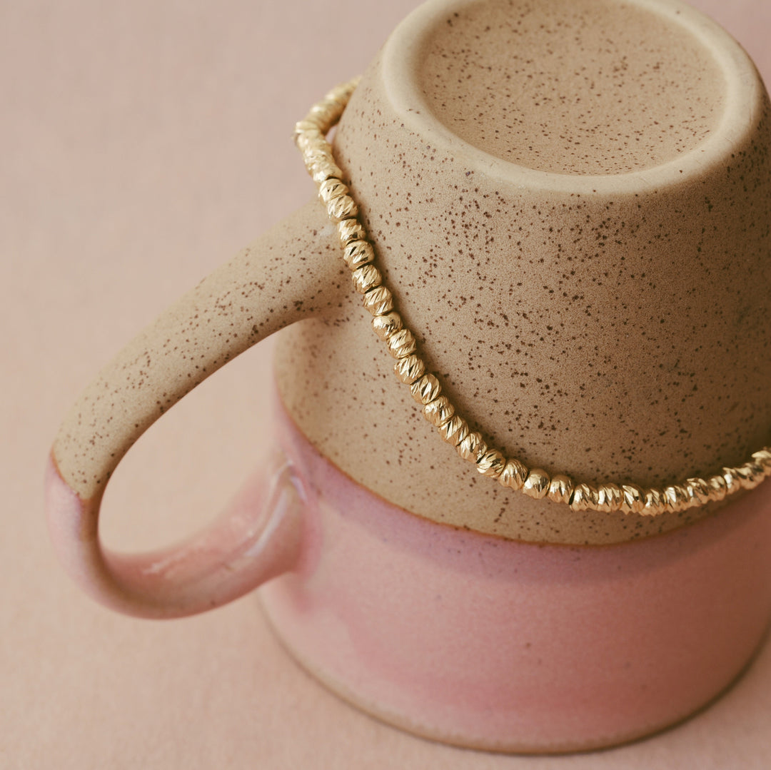 Goldenes Edelstahl-Bracelet mit brushed Perlen um eine Tasse gespannt