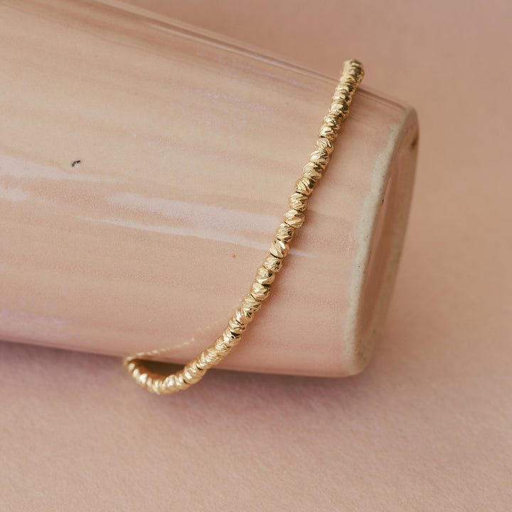 Goldenes Edelstahl-Bracelet mit gebürsteten Perlen um liegende Keramik