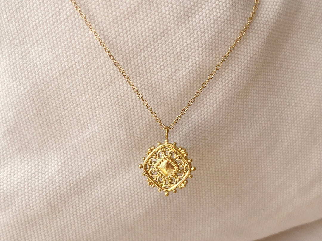 Goldene Halsketten mit Rauten Anhänger vor blassrosafarbenem Hintergrund