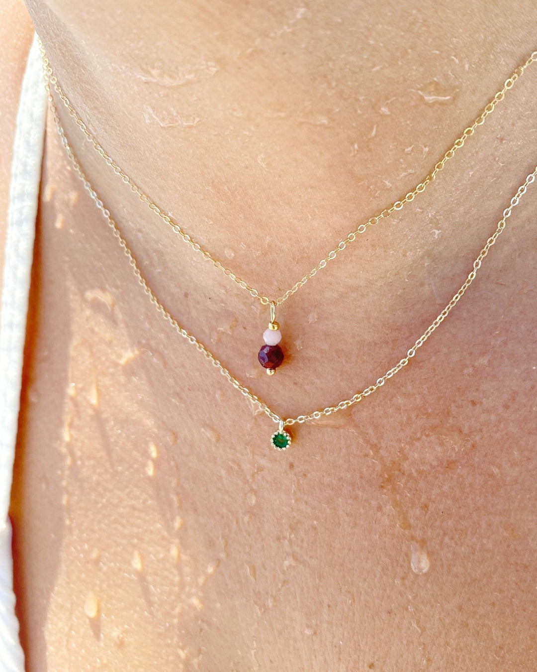 Goldene Halskette mit grünem Kristall und goldene Kette mit roter und rosafarbener Perle an Model
