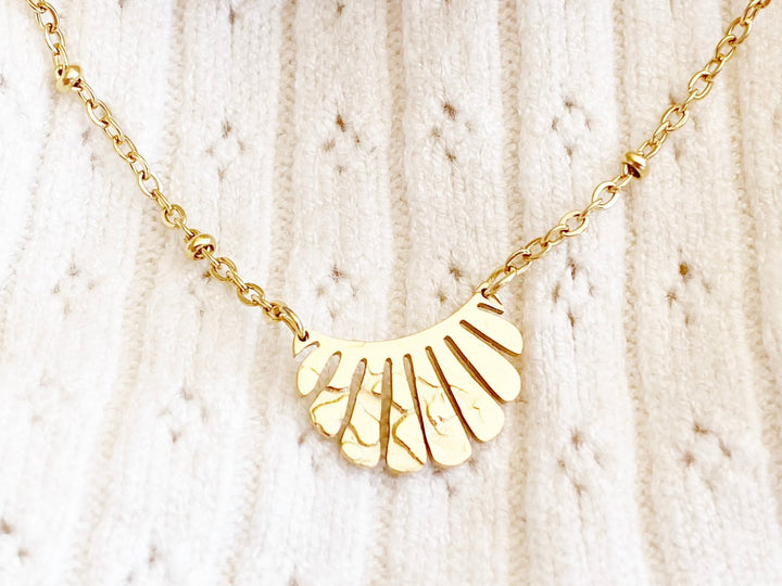 Goldenes Armband mit Anhänger vor weißem Stoff