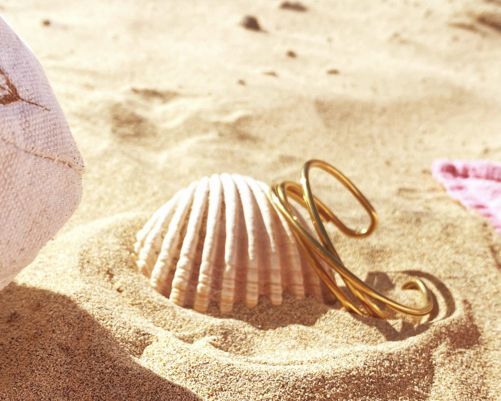 Gewickelte Armspange vergoldeter Edelstahl Detailansicht im Sand an einer Muschel gelehnt - ALICIA'S DIARY®