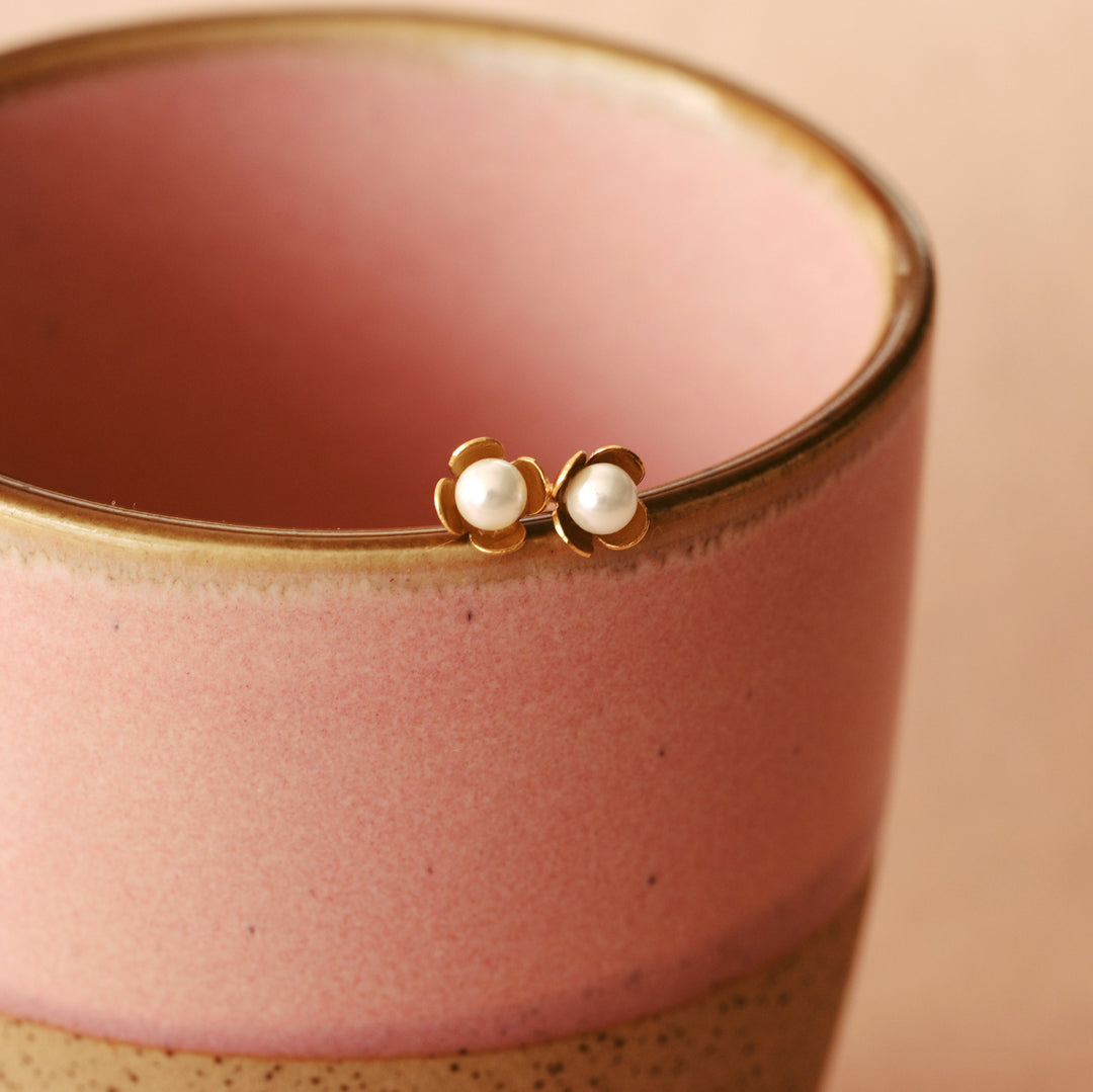 Goldene Blüten Ohrstecker mit Süßwasserperlen am Rand einer rosa Tasse