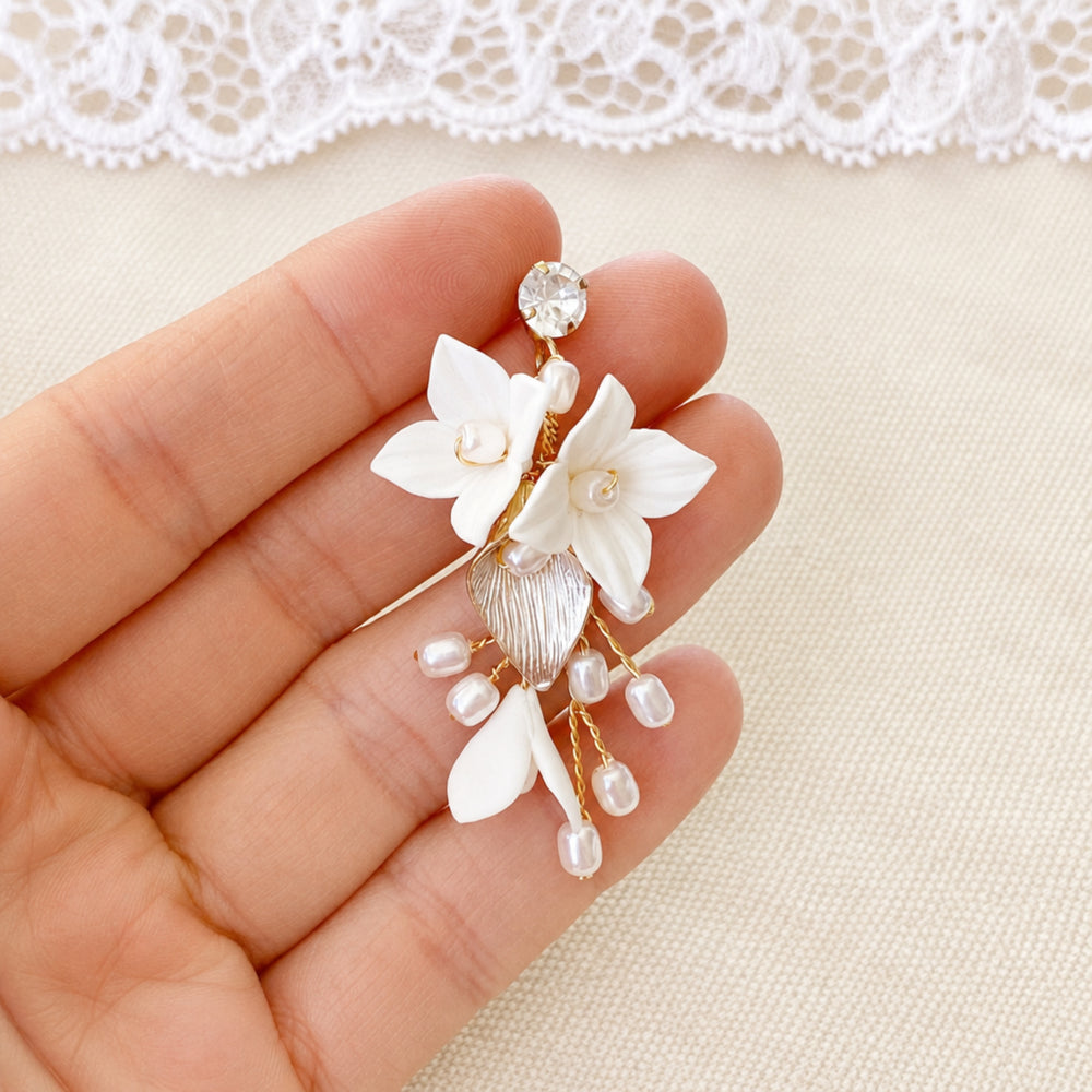 Boucle d'oreille de mariée Lisa à fleurs blanches et perles tenue dans une main