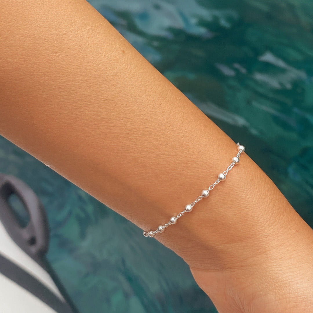 Silbernes Satelliten-Armband mit Kugelperlen getragen am Handgelenk vor Poolwasser