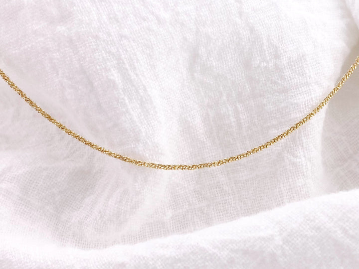 Minimalistische goldene Halskette vor weißem Tuch