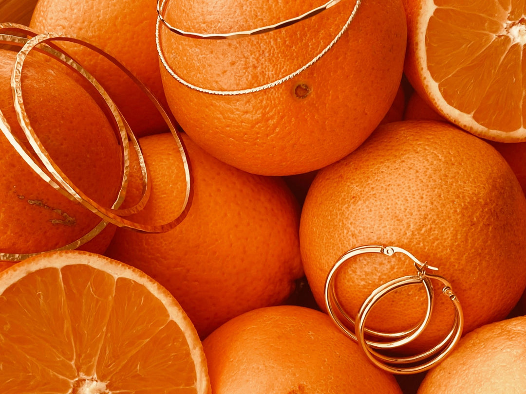 Armreifen aus Gold mit geometrischer Struktur und doppelte Creolen auf aufgeschnittenen Orangen