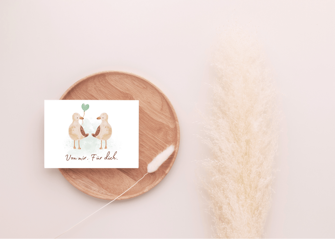 Carte cadeau motif oiseau marin posée sur un plateau rond en bois avec une fleur séchée