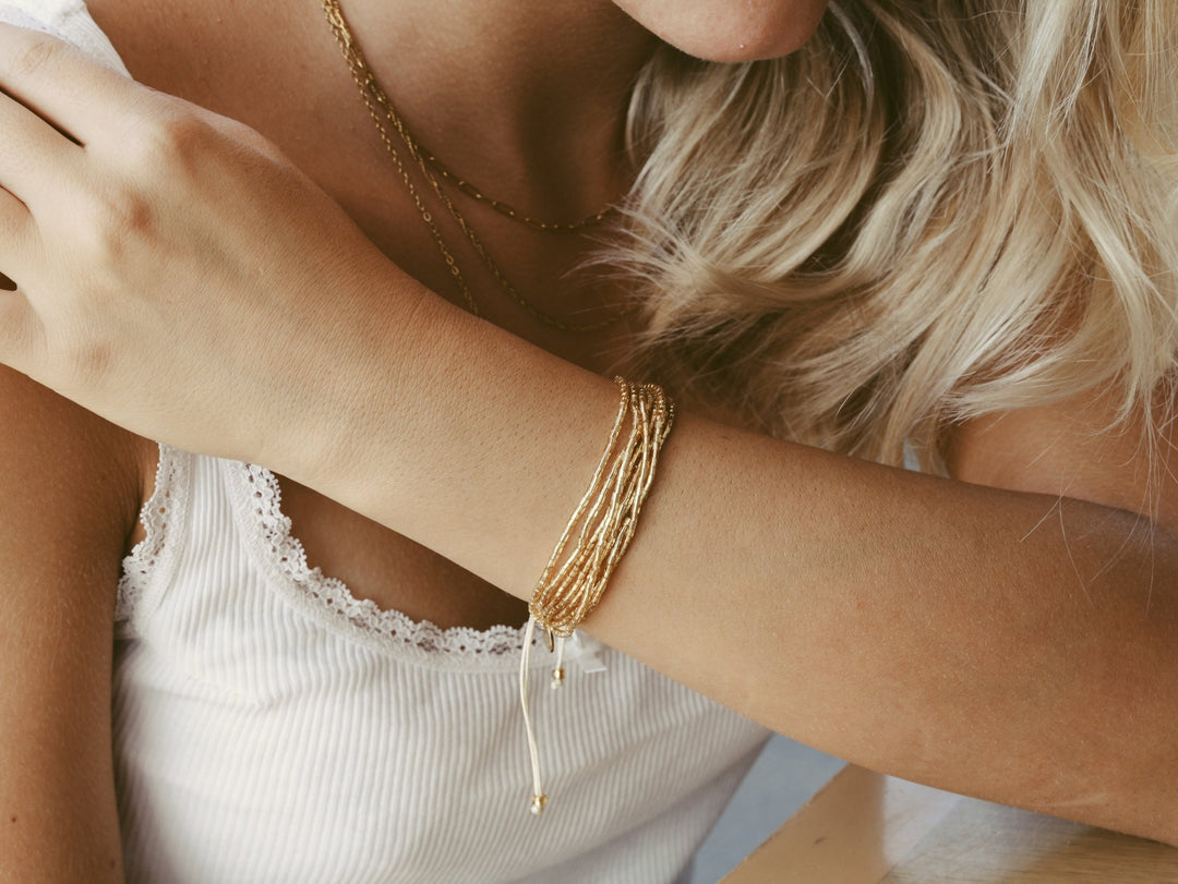 Goldenes Glasperlen-Armband, Edelstahl Layering Kette an blonder junger Frau mit weißem Spitzen-Top, Schmuck von Alicia&