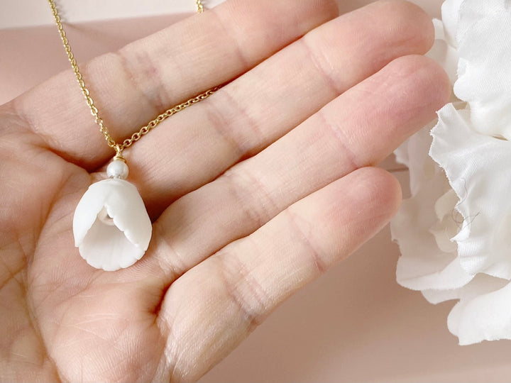 Collier de mariée doré avec fleur blanche et perle tenu dans la main pour comparer la taille