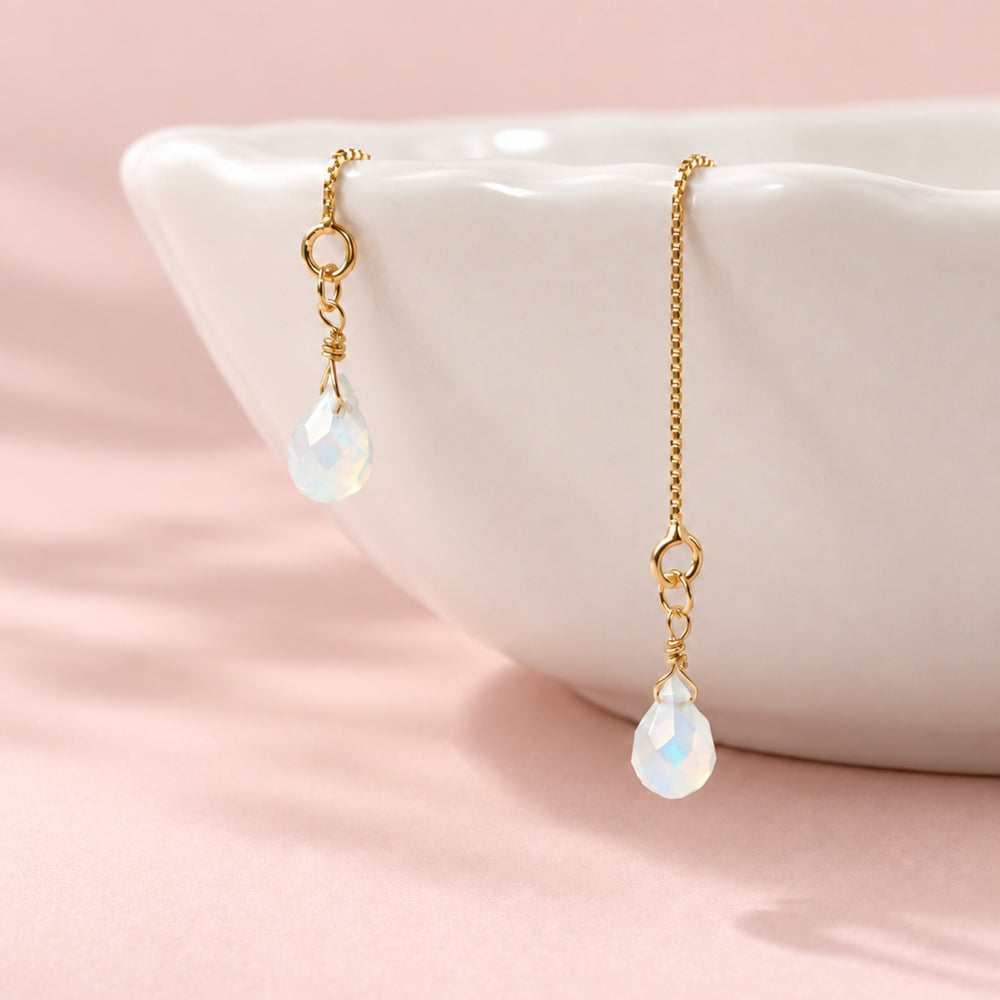 Filigrane goldene Fädelohrringe mit milchig blauem Kristall an weißer Schale