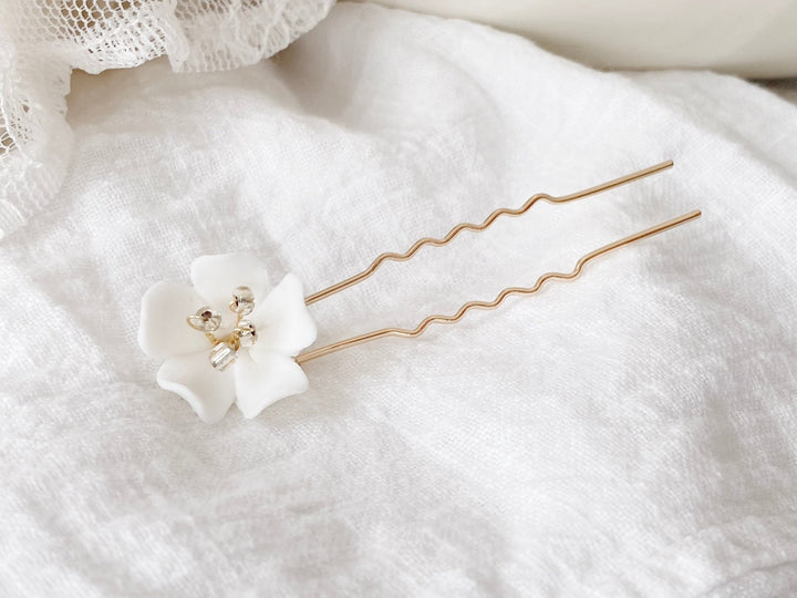 Gold hair pin with a handcrafted white flower on textured white fabric