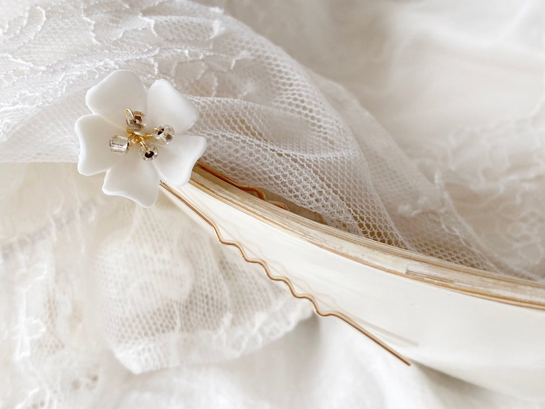 Gold hair pin with a white flower draped on a white bowl with lace