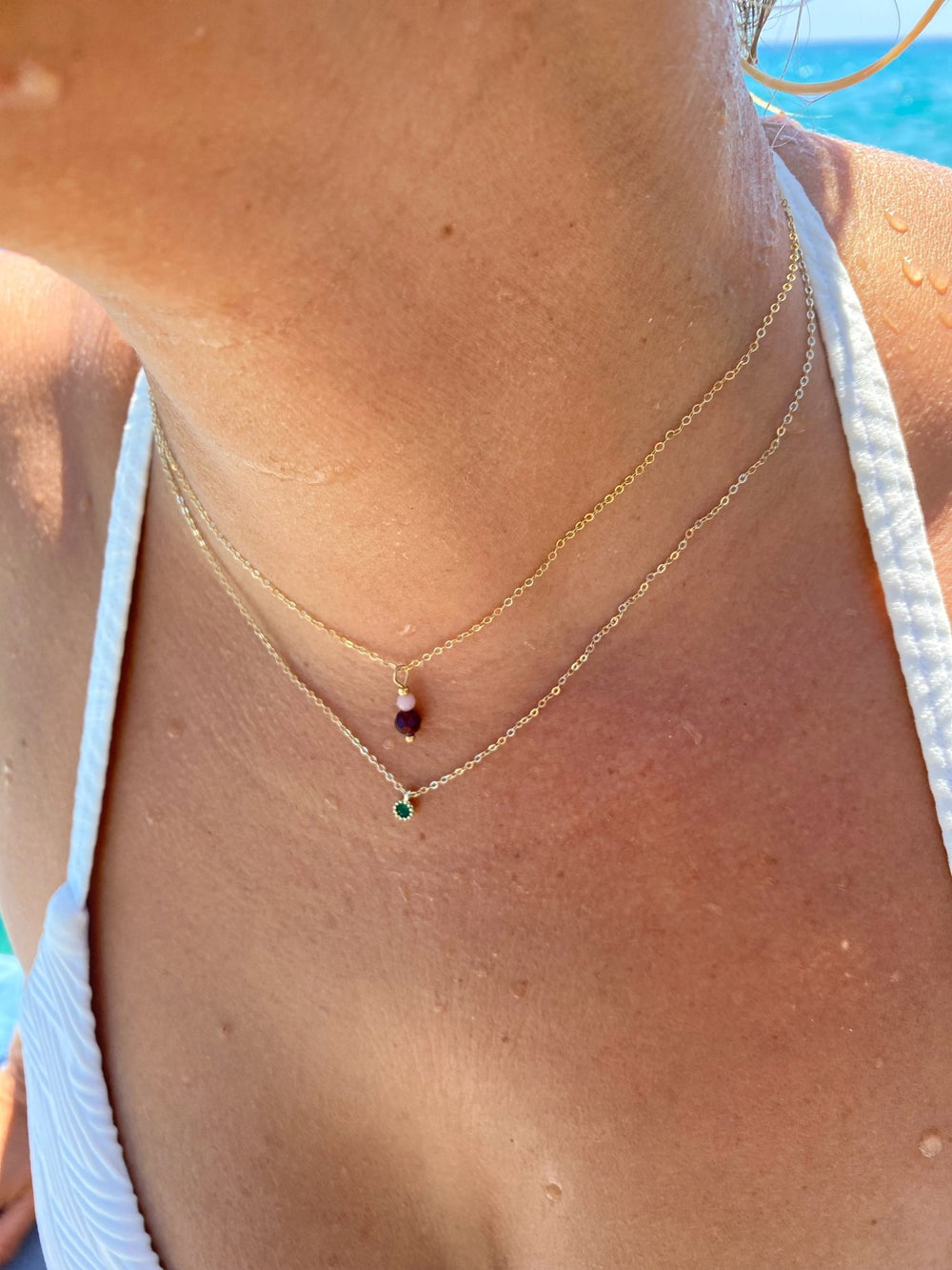 Goldene Halskette mit grünem Kristall und goldene Kette mit roter und rosafarbener Perle an Model