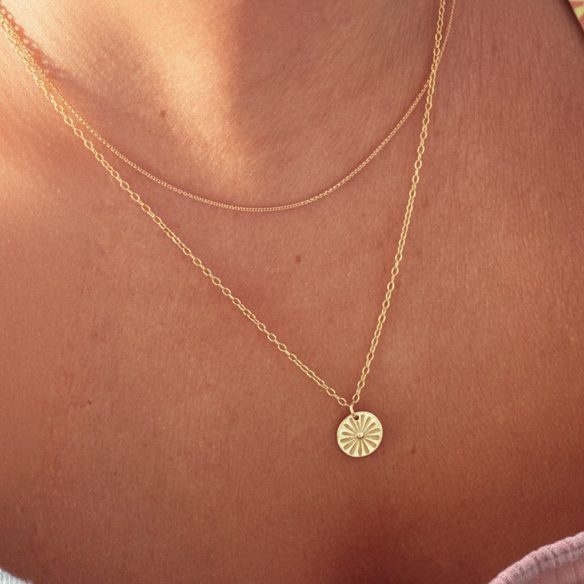 Un delicado collar con forma de sol que se luce en la playa durante el verano.