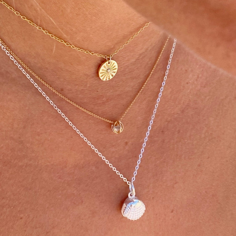 Joyas superpuestas: Un collar dorado con forma de sol combinado con otros collares.