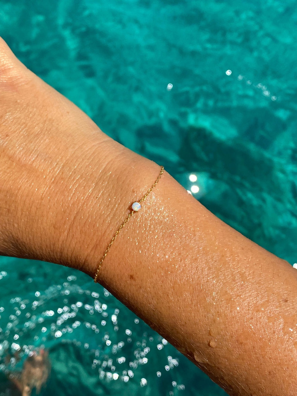 Goldenes Armband mit Opal an Model vor Meerwasser, wasserfester Schmuck mit Opal Steinen für den Sommer - ALICIA'S DIARY