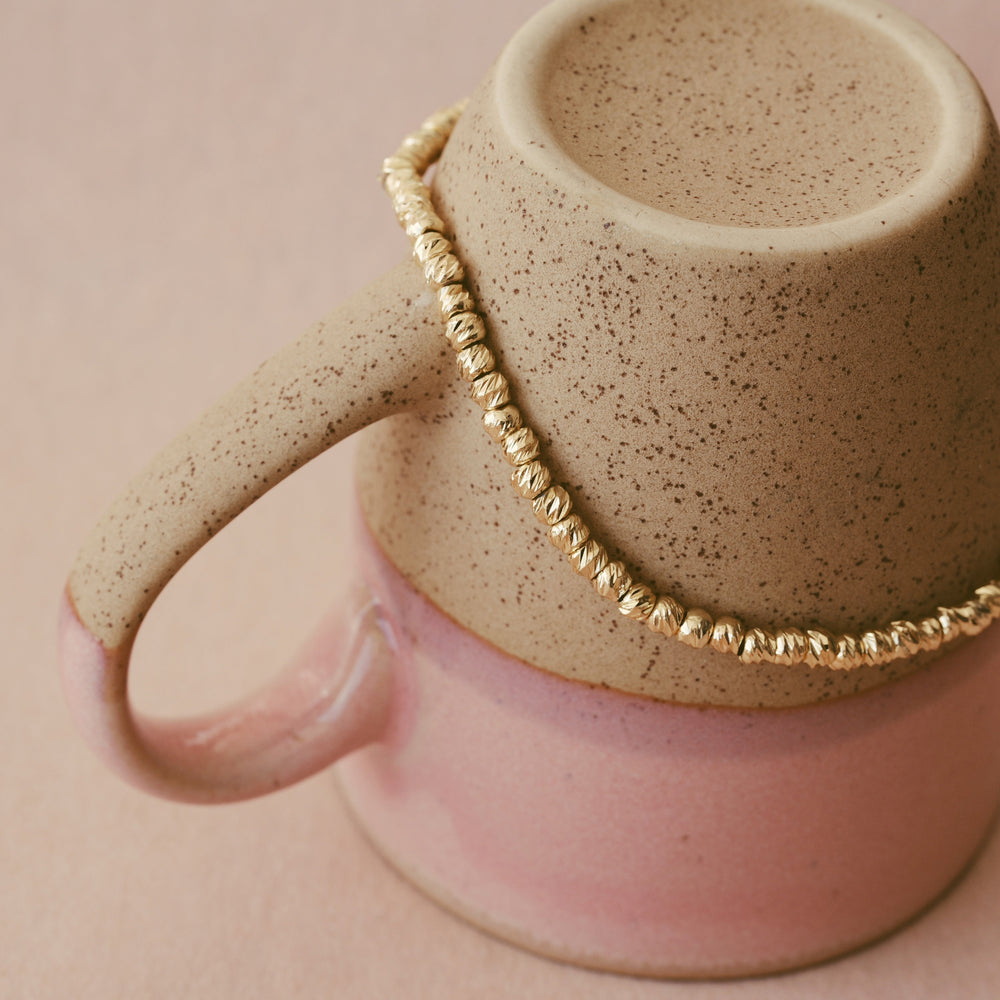 Gold stainless steel bracelet with brushed beads stretched around a cup