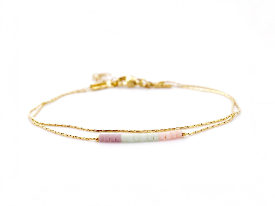 Goldenes Armband mit zwei Bändern und lila, grünen und rosa Miyuki Perlen vor weißem Hintergrund