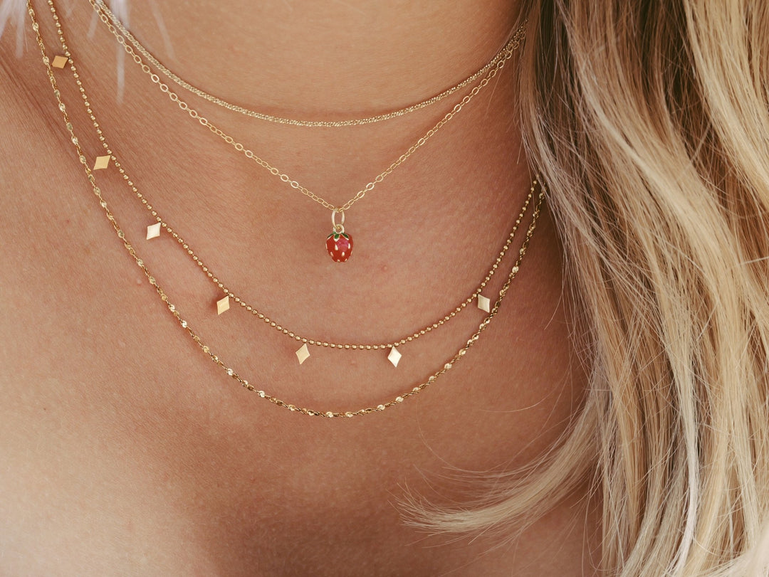 Necklace Stacking gold Inspo, Edelstahl Schmuck, Erdbeerschmuckan blonder junger Frau mit grünem Spaghettiträger Top und Spitzen-BH