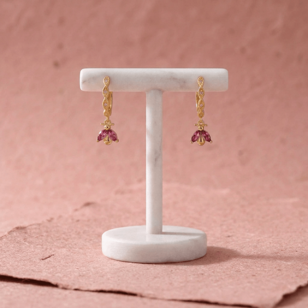 Goldene Kinder Creolen mit rosa pinken Glitzersteinen, hängend an einem weißen Marmor Schmuckständer auf rosa Papier