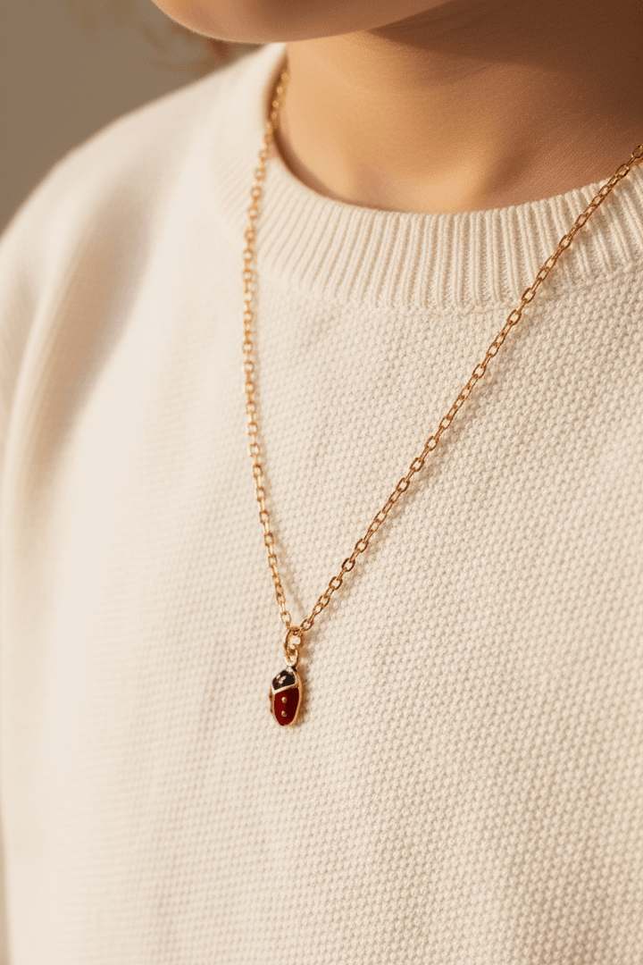 Marienkäfer Halskette getragen von Kind mit rosa Pulli, schöner goldener Kinderschmuck von Alicia&