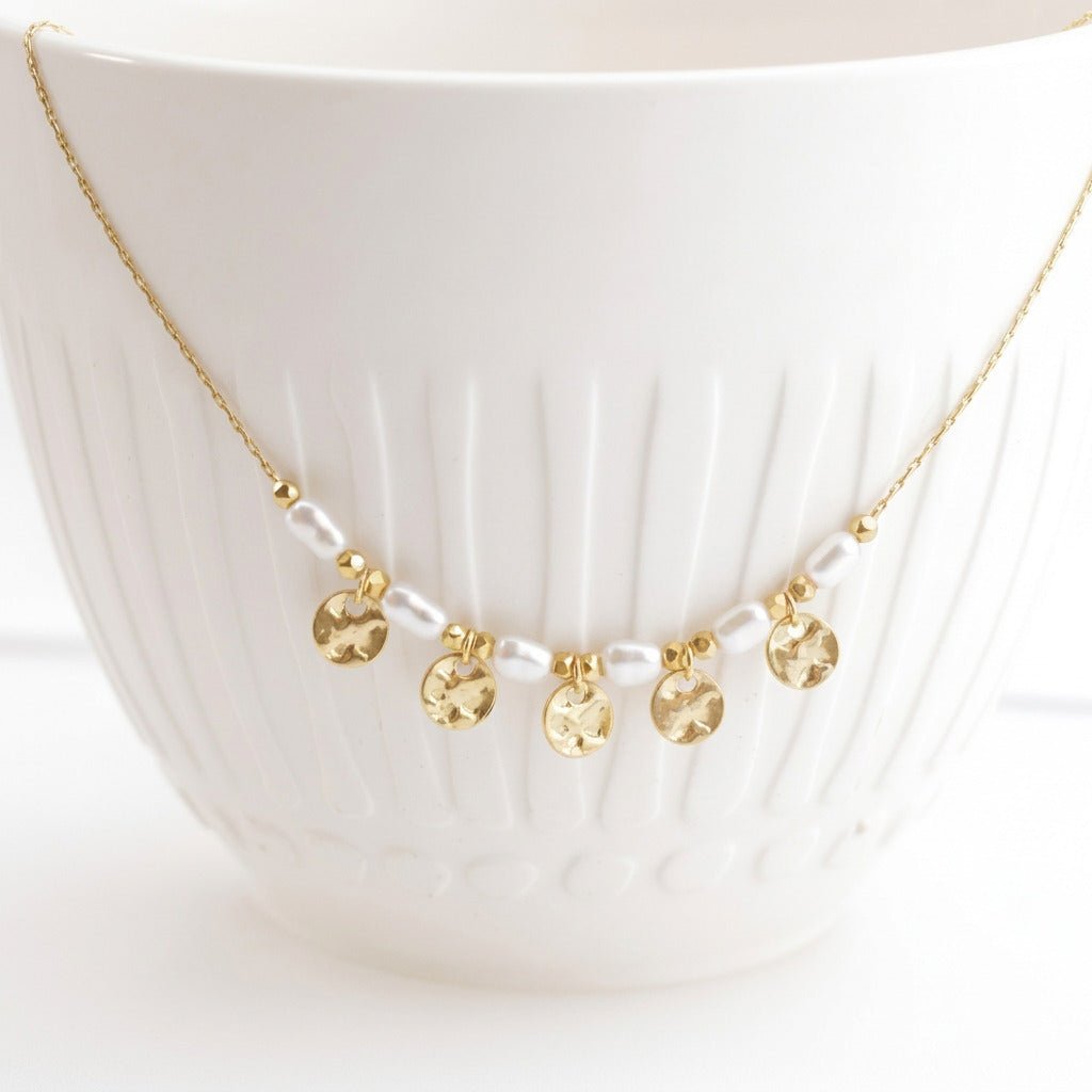 Close-up of the Coins and Pearls necklace with hammered discs on a white ceramic cup