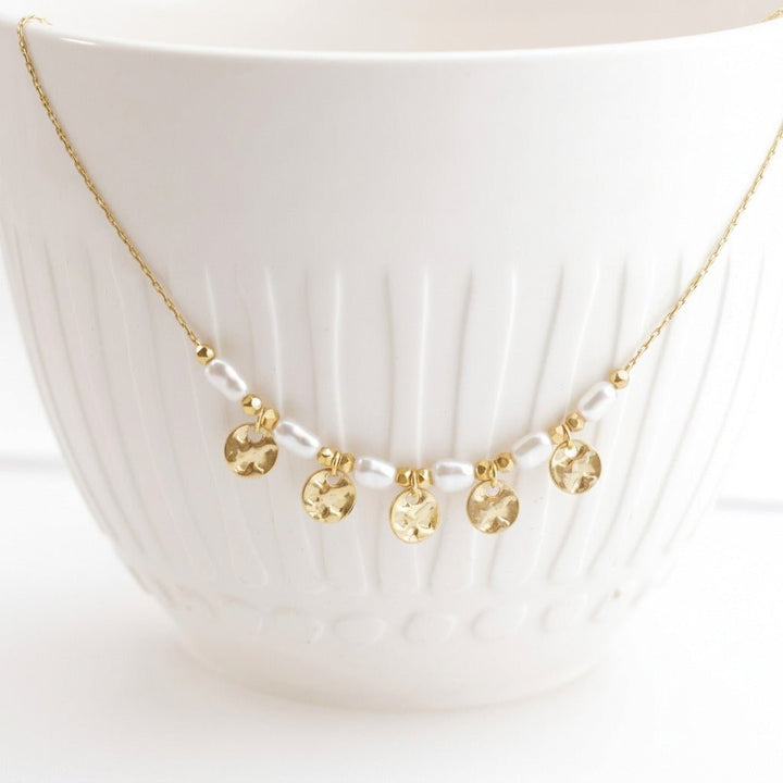 Close-up of the Coins and Pearls necklace with hammered discs on a white ceramic cup