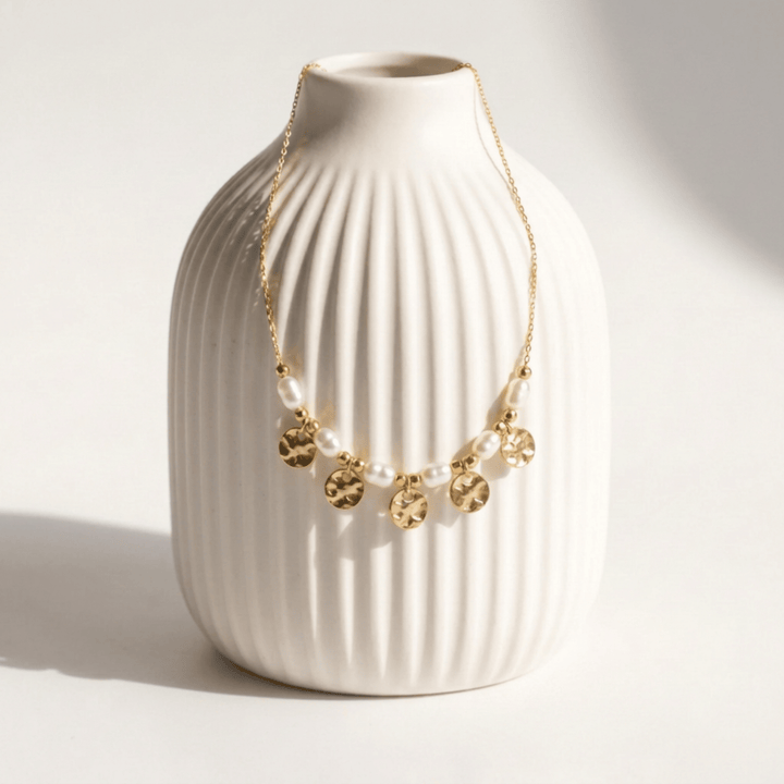 Coins and Pearls necklace with freshwater pearls draped on a white ribbed ceramic vase