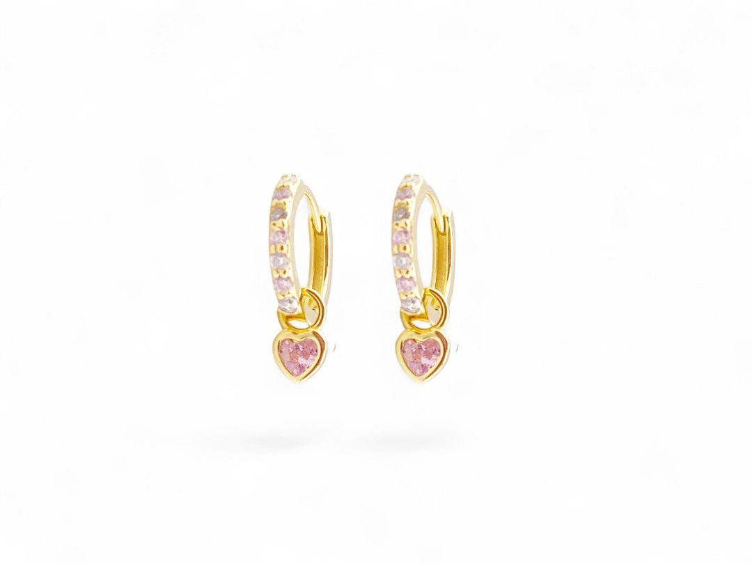 Goldene kleine Creolen mit rosa Glitzerstein und Herz vor weißem Hintergrund