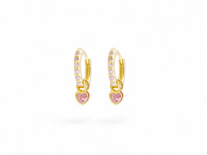 Goldene kleine Creolen mit rosa Glitzerstein und Herz vor weißem Hintergrund