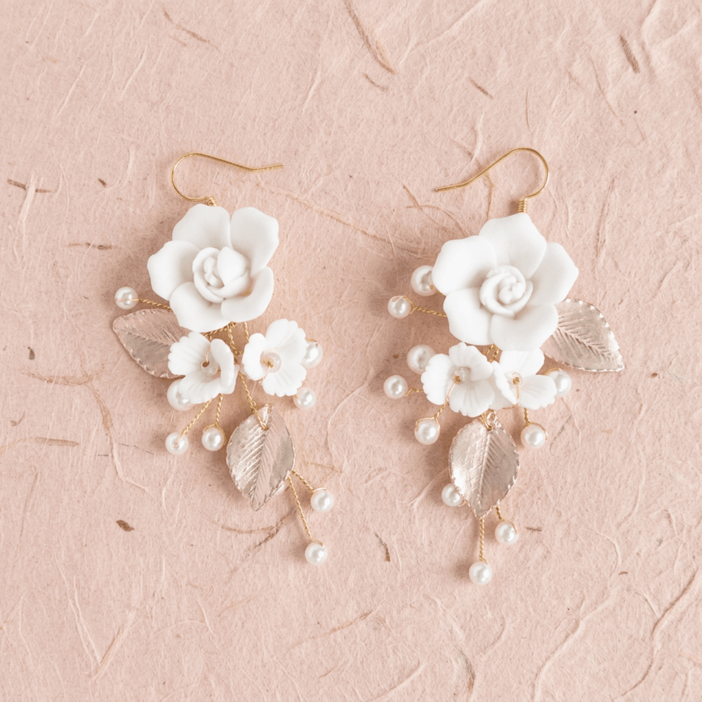 Weiße Blumenohrringe Rosalie mit Perlen und Blättern auf beigem Naturpapier