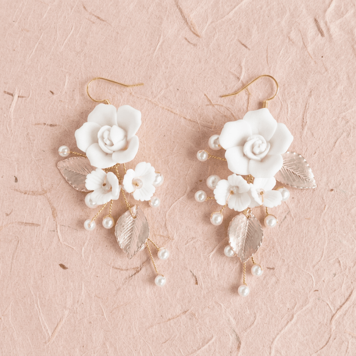 Weiße Blumenohrringe Rosalie mit Perlen und Blättern auf beigem Naturpapier