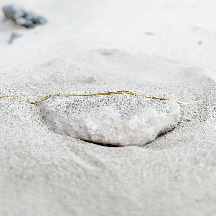 Wasserfester Schmuck für Strand, Meer und Pool, goldenes Armband im Sand auf Stein