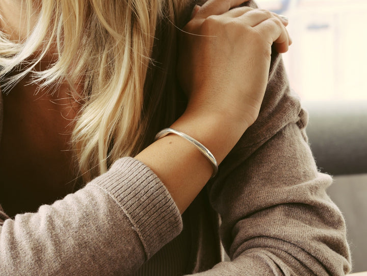 Silber Armcuff an junger Frau mit blonden langen Haaren und brauner Strickjacke, schöner Silberschmuck
