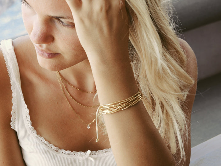 Goldener Schmuck an schöner junger Frau mit blonden Haaren und weißen Spitzen-Oberteil, Armband und Kette von Alicia&