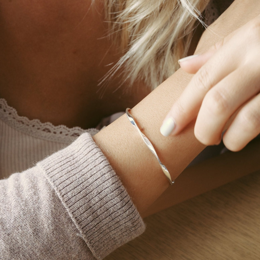 Twisted echt silberne Armcuff für schmale Handgelenke aus 925 Silber an junger Frau in hellbrauner Strickjacke mit grauem Nagellack