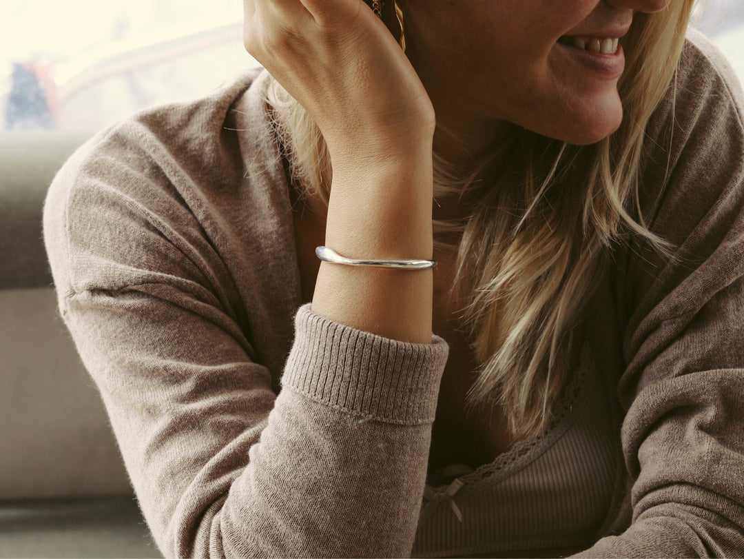 Organic Armcuff silber und gedrehte twisted Creolen gold an junger lachender Frau mit blondern Haaren und kaffeeebrauner Strickjacke